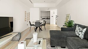 A modern living room with a flat-screen TV, a gray sofa, a coffee table, and a dining area with a white table and chairs.