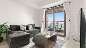 A modern living room with a grey sofa, a coffee table, and a view of a balcony with outdoor furniture.