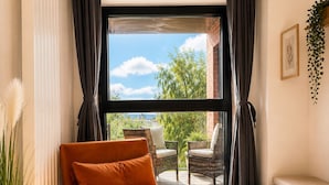 A modern living room with a sofa, a small table with a lamp, a bench, and a view of greenery outside. - PrivateTerrace Opposite PiccadillyLine • 20min SOHO, Oxford Street & Sightseeing (Uxbridge)