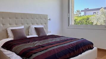 A modern bedroom with a large bed, a tufted headboard, and a view of a building through a window.