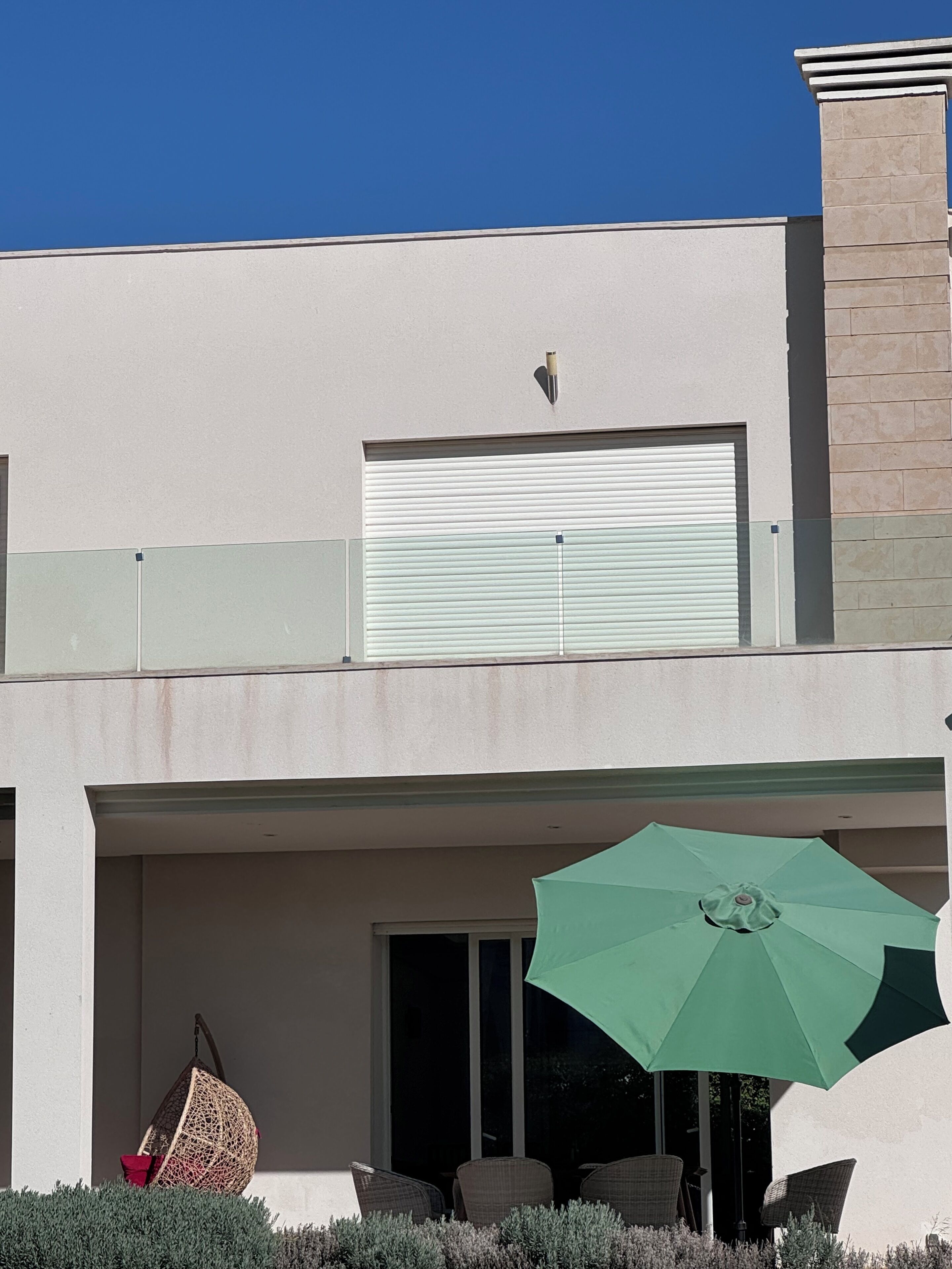 A modern two-story house with a covered patio area featuring outdoor furniture and a green umbrella.