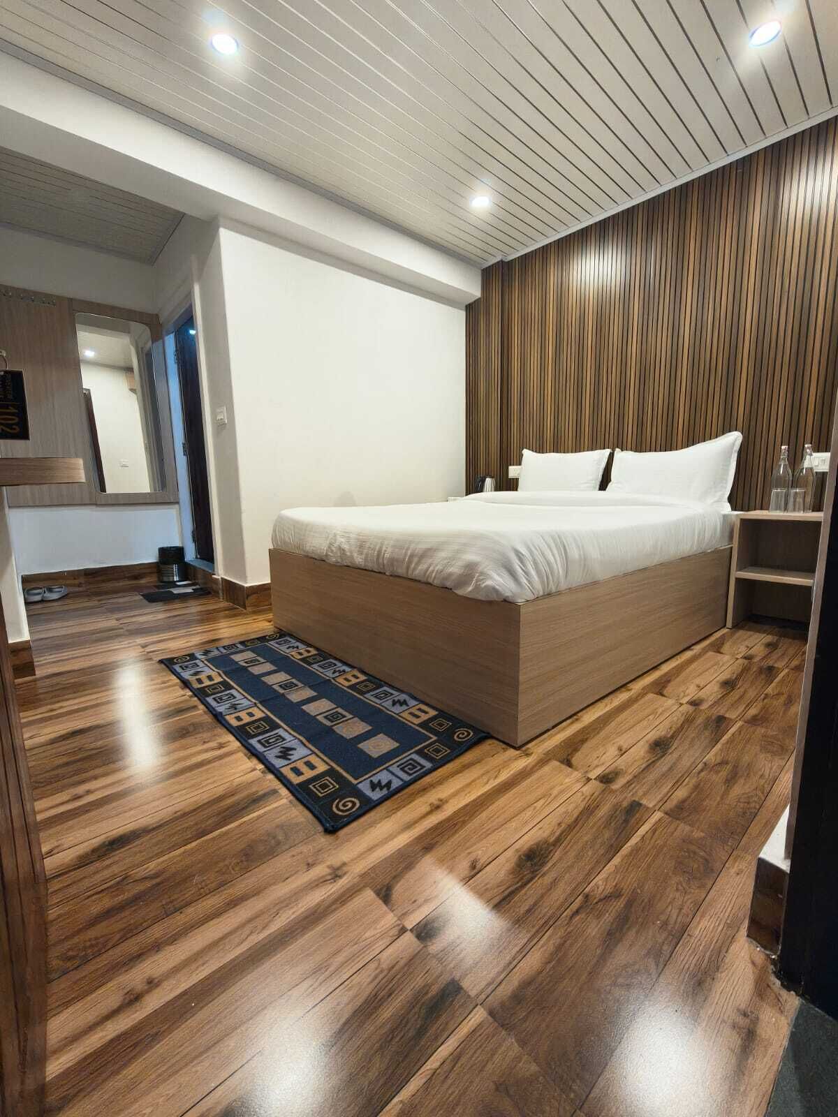 A modern bedroom with a wooden floor, a bed with white linens, a wooden headboard, and a small bedside table.