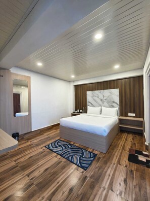 A modern bedroom with a wooden floor, a bed with a marble headboard, a nightstand, and a wall-mounted mirror. - PINEVIEW ESCAPES (Darjeeling)