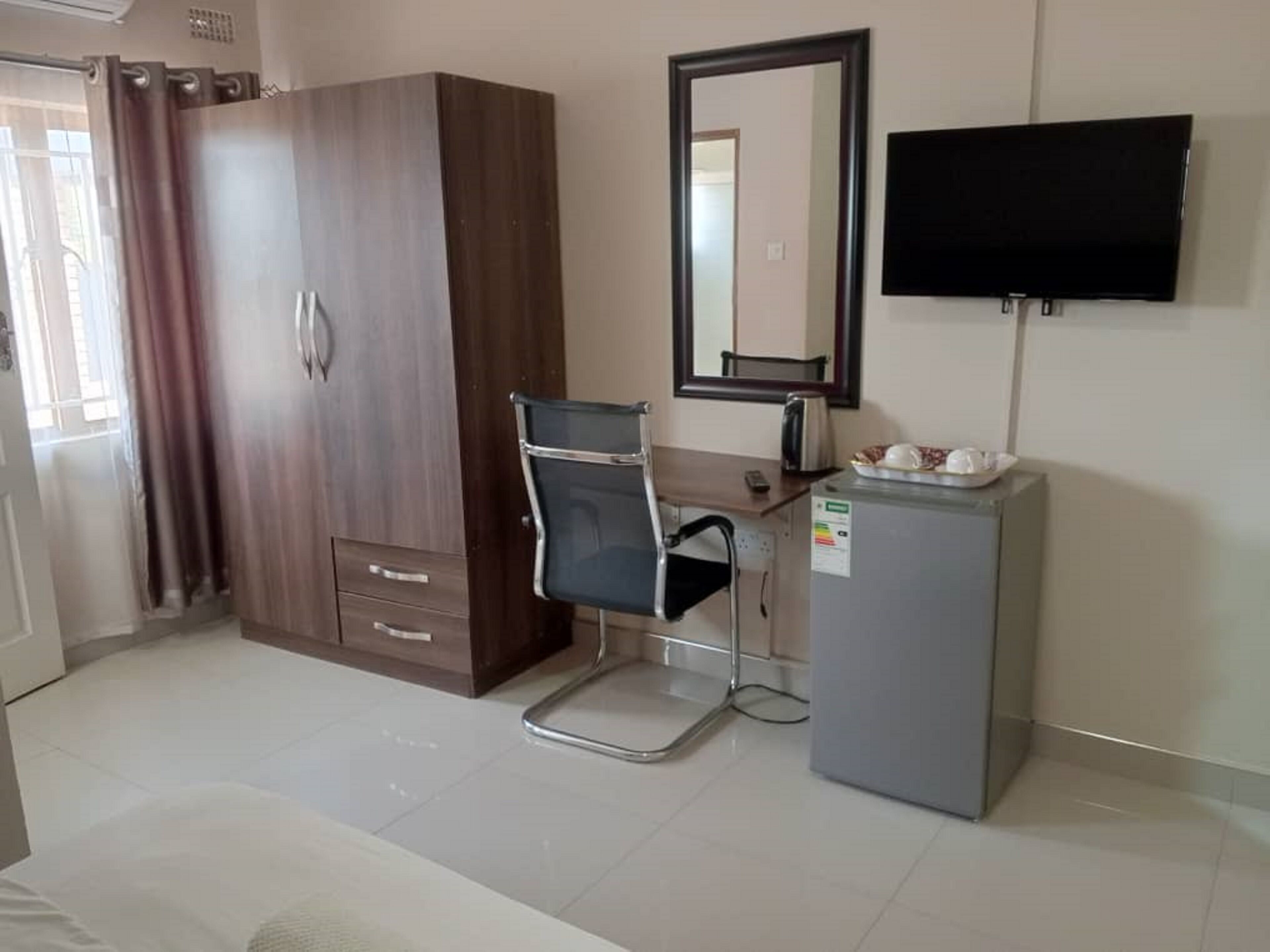Una habitación de hotel con armario, escritorio y silla, televisión y un refrigerador pequeño.