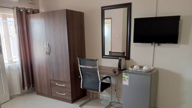 A hotel room with a wardrobe, a desk with a chair, a television, and a small refrigerator. - North Stay Inn (Livingstone)