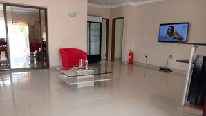 A spacious living room with a glass coffee table, a red armchair, and a television on the wall. - North Stay Inn (Livingstone)