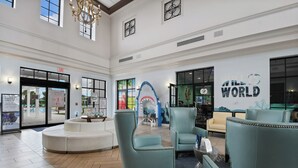 A spacious lobby with a high ceiling, a central seating area with armchairs, a large mural, and a sign reading 'THE WORLD'. - Cinderella’s Castle Retreat, Private Pool, Pokémon Room, Minutes to Disney! (Four Corners)