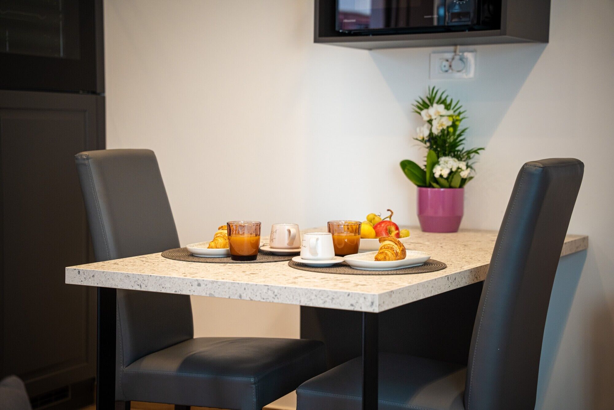 A dining area with a table set for breakfast, including croissants, coffee, and fruit.