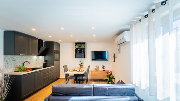 Eine moderne Küche mit dunklen Schränken, einer Marmorarbeitsplatte und einem Essbereich mit einem Holztisch und einem blauen Sofa.