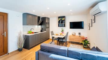 A modern kitchen with grey cabinets, a dining area with a table and chairs, and a living area with a blue sofa.
