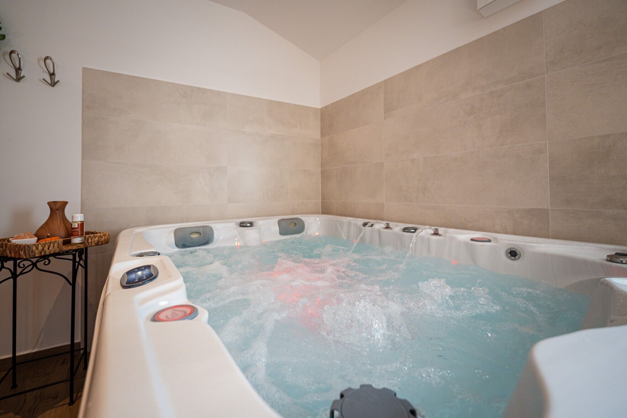 A hot tub in a room with beige tiled walls and a wooden floor.