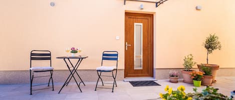 Zona d'estar a l'aire lliure amb dues cadires, una taula, una porta i plantes en testos.