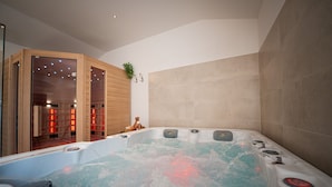 Ein modernes Badezimmer mit einer großen Badewanne, Holzdetails und einem sichtbaren Saunabereich.