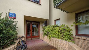 Entrada de um edifício com uma bicicleta estacionada, uma placa indicando 'Ul. Drawska 14F' e um muro de tijolos com vegetação.