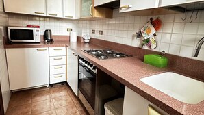 Une cuisine avec des meubles blancs, un four à micro-ondes, une cuisinière à gaz et un évier.