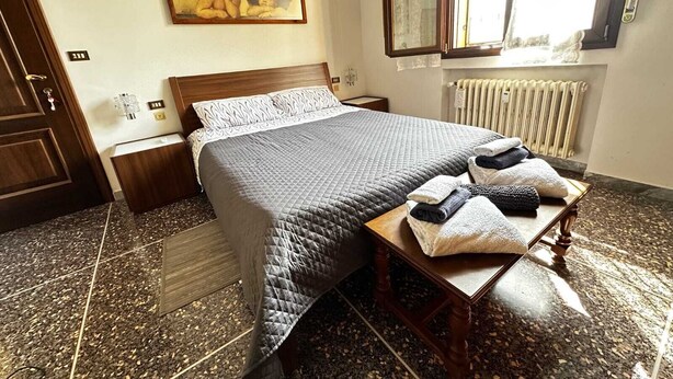 Un lit bien fait, recouvert d’une courtepointe, une table de chevet avec des serviettes, une commode, un tableau accroché au mur et une fenêtre donnant sur un beau paysage.