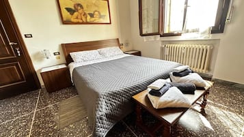 Un letto rifatto con una coperta, un comodino con asciugamani, una lampada da notte, un quadro appeso al muro e una finestra con vista.