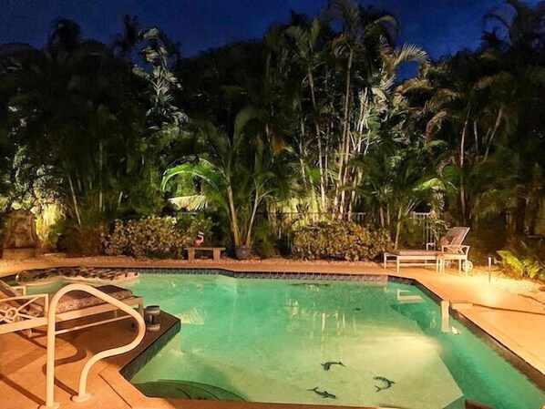 A swimming pool with clear water, surrounded by lush tropical vegetation and a few lounge chairs.