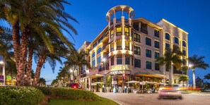 A hotel with a curved facade, outdoor seating, and palm trees.