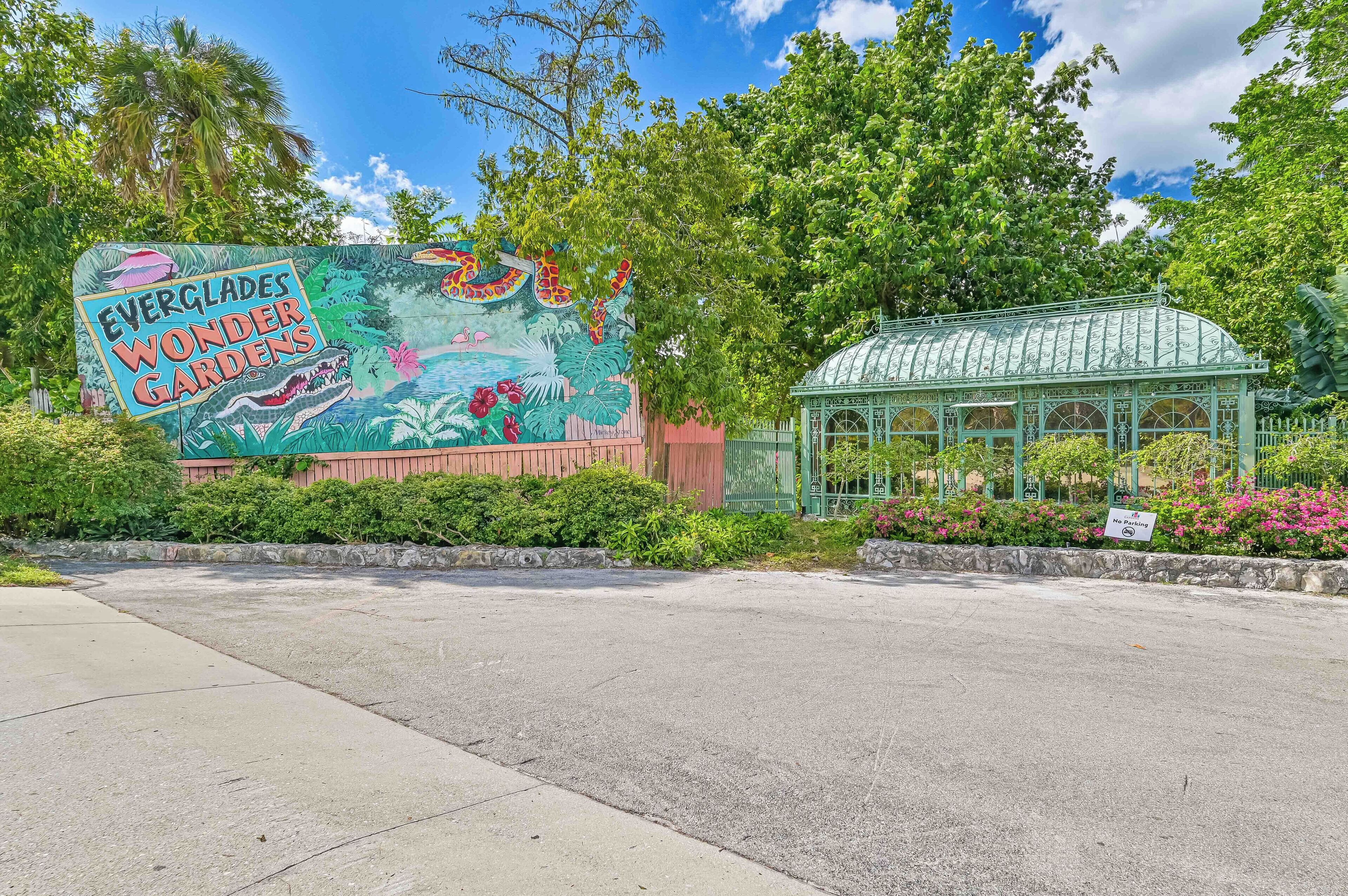 A sign for Everglades Wonder Gardens with a mural of tropical plants and a greenhouse structure.