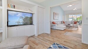 Una sala de estar con un televisor de pantalla plana, armarios blancos, un sofá y una mesa de centro.