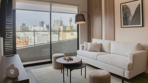 A modern living room with a large window, a white sofa, a round coffee table, and a floor lamp. - w Charming 2BR w Balcony in Miraflores (Lima)