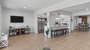 A modern kitchen with white cabinetry, a stainless steel refrigerator, and a dining area with wooden stools. - Relaxing Paradise Hills Retreat 4 Bedroom Home (San Diego)