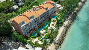 A multi-story hotel with a swimming pool, surrounded by palm trees and a beach.