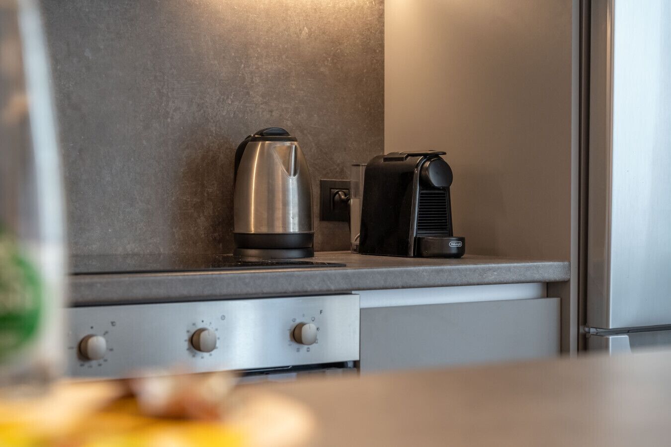 A kitchen with a stainless steel kettle, a black coffee maker, and a modern countertop.
