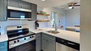 Una cocina moderna con gabinetes grises, un microondas de acero inoxidable, horno empotrado y lavavajillas.