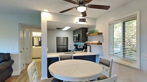 Una cocina moderna con una isla central, un comedor con una mesa redonda y sillas, y un ventilador de techo.