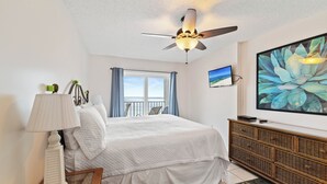 A bedroom with a bed, a ceiling fan, a TV, and a large window with curtains.