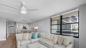 Un salon moderne avec un canapé d’angle, une table basse et une grande fenêtre donnant sur l’extérieur.