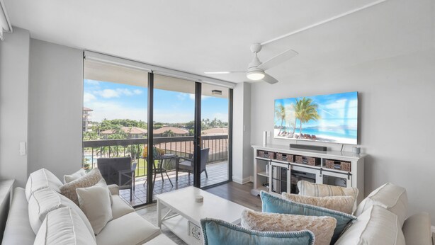 Un salon moderne avec un canapé blanc, une table basse et un téléviseur posé sur un meuble blanc. Il y a un balcon avec vue sur la ville.