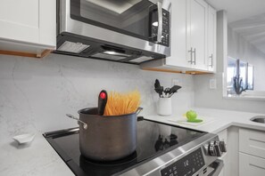 A modern kitchen with a stove, a pot with spaghetti, a microwave, and white cabinets.