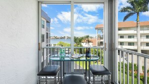 Uma varanda com mesa de vidro e duas cadeiras, com vista para a água e edifícios.