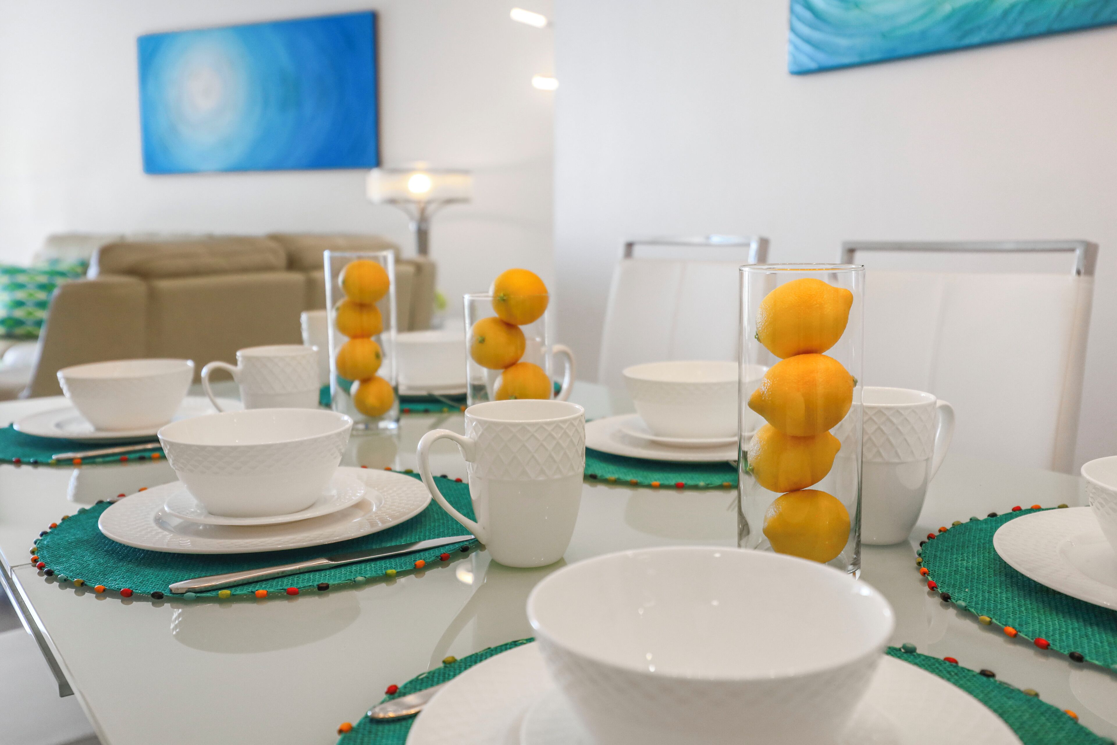 A dining table set with white dishes, a clear glass vase with orange slices, and a green placemat.