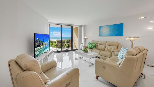 Een moderne woonkamer met een grote televisie, beige banken, een salontafel en een balkon met uitzicht.