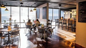A restaurant with high tables and chairs, large windows offering a view, and a menu board on the wall.