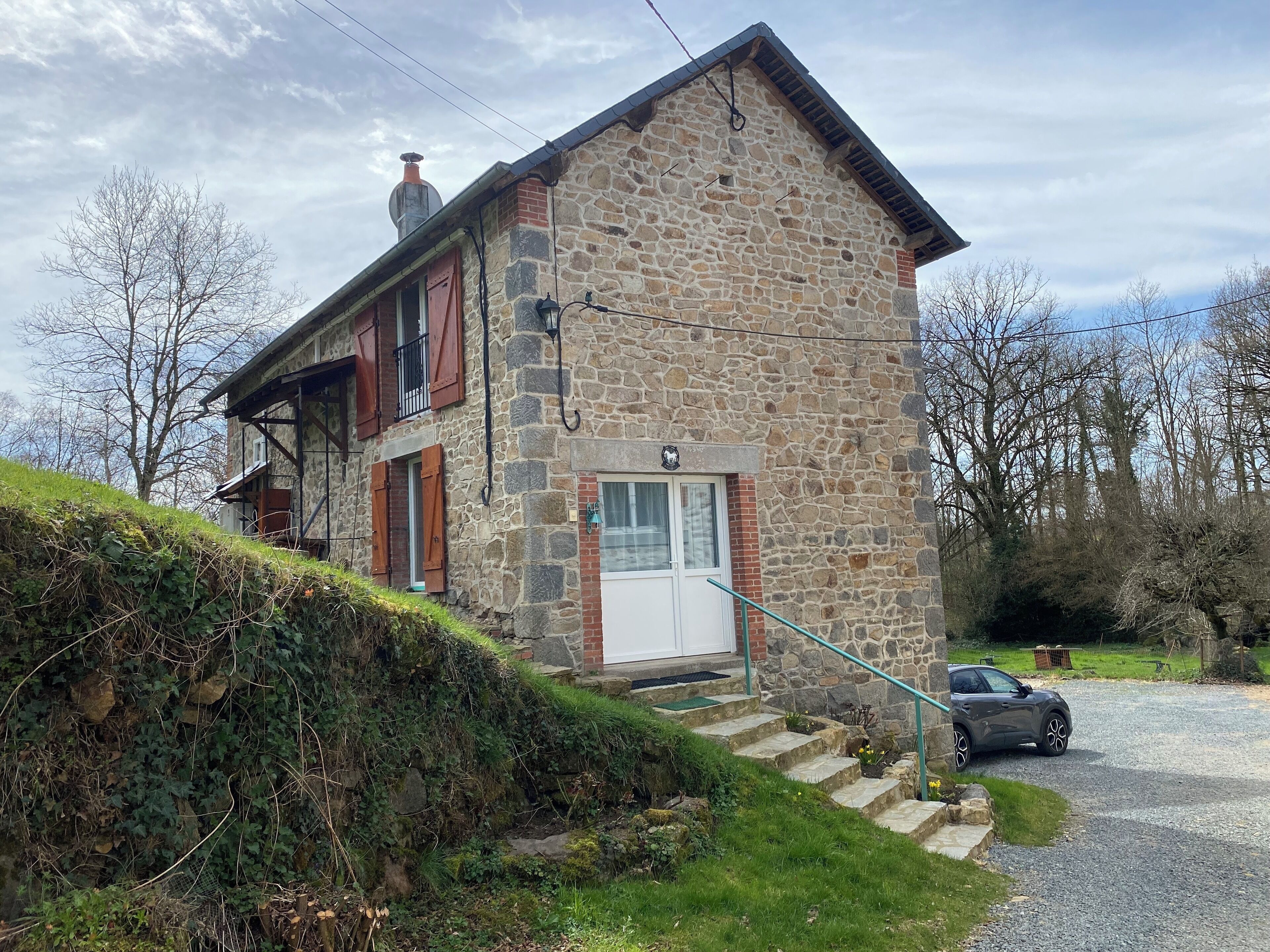 Un bâtiment en pierre avec un toit en pente, un escalier en bois et une voiture garée devant.