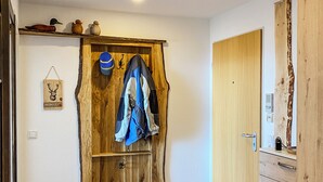 A wooden door with a coat rack and a sign, a grey mat, a wooden bench, and a trash can.