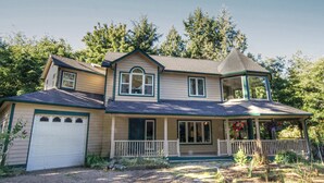 Une maison à deux étages avec un garage, une véranda dotée d’une balustrade et une petite structure en forme de tour sur le toit.