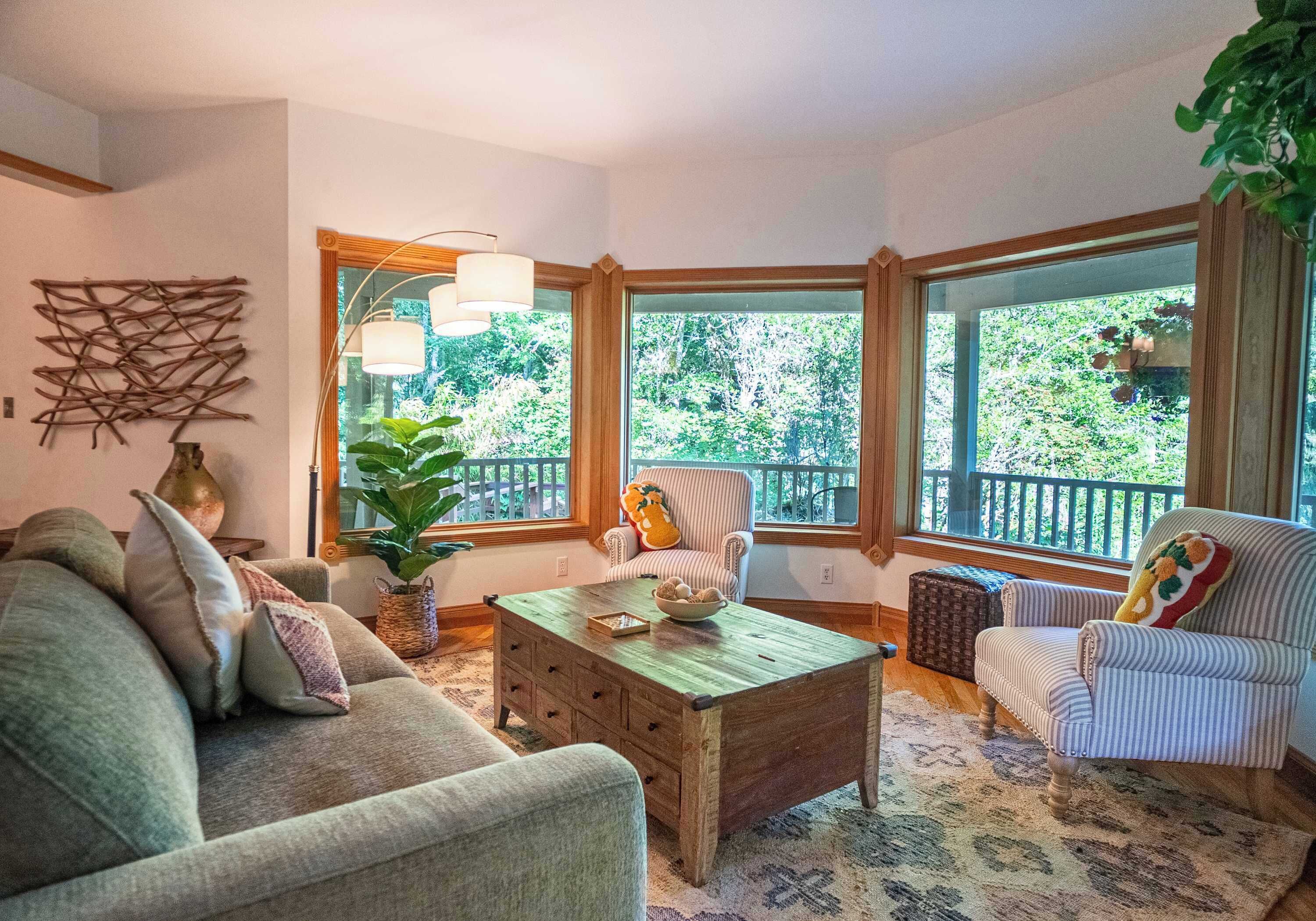 A cozy living room with a wooden coffee table, striped armchairs, and a large window offering a view of greenery.