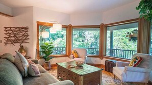 Un salon chaleureux avec une table basse en bois, des fauteuils à rayures et une grande fenêtre donnant sur un paysage verdoyant.