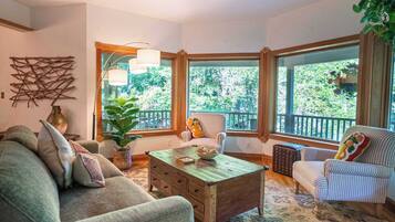 A cozy living room with a wooden coffee table, striped armchairs, and a large window offering a view of greenery.