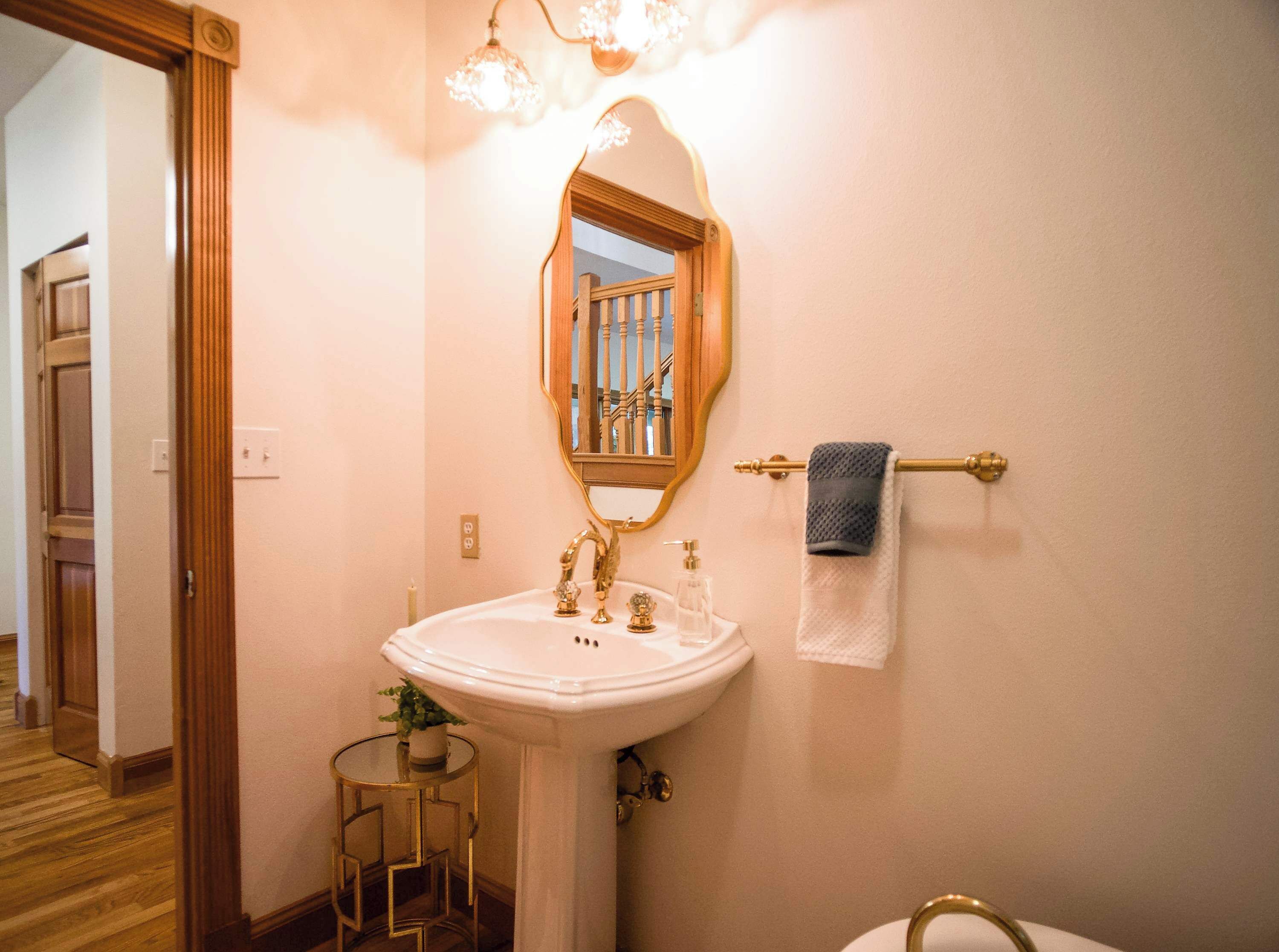 A bathroom with a white sink, gold fixtures, a mirror, and a towel rack.