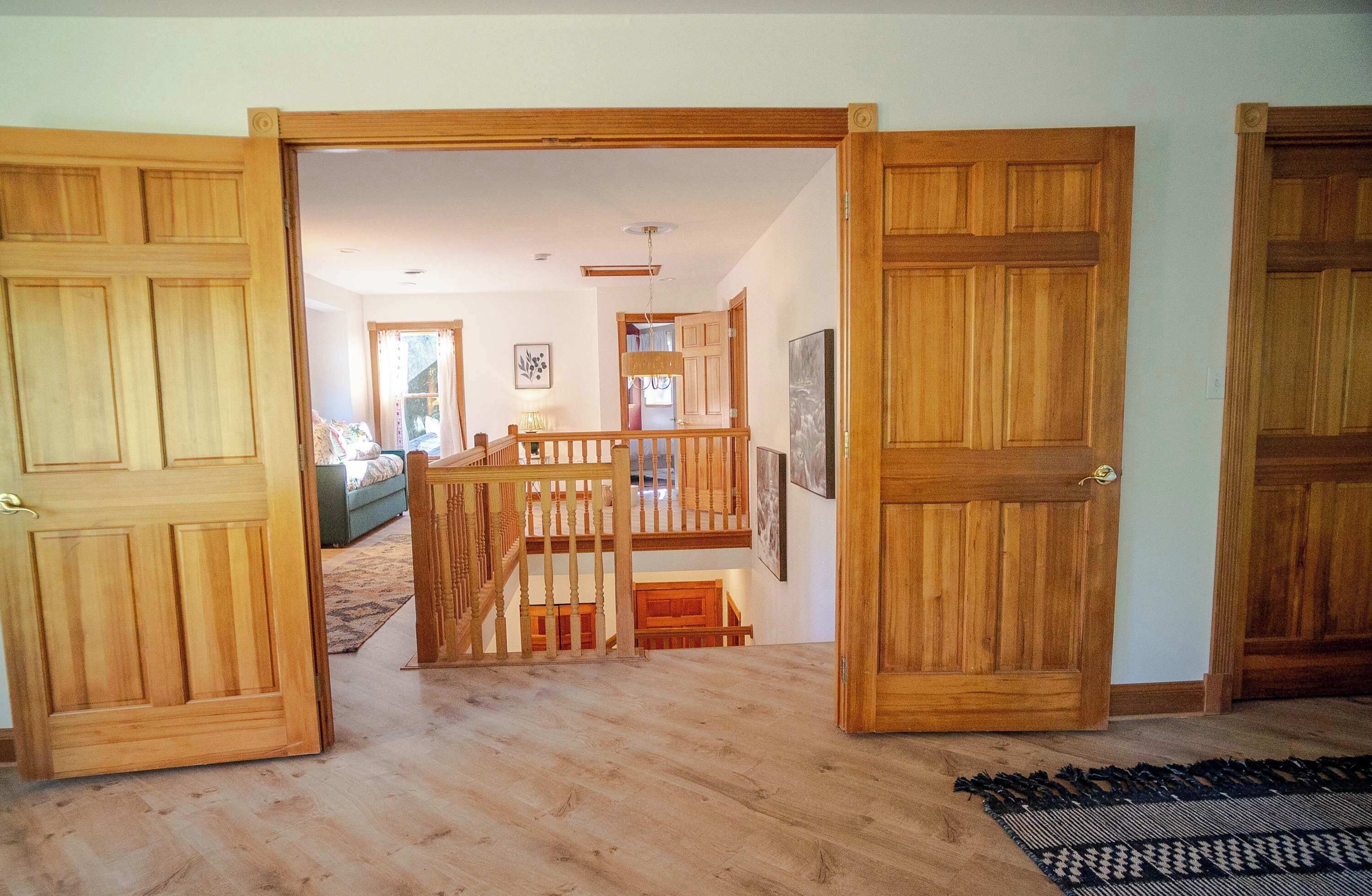 A wooden-floored hallway with open doors leading to a living area with a sofa and a staircase.