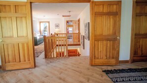 Un couloir au plancher de bois, avec des portes ouvertes donnant sur un espace de vie comprenant un canapé et un escalier.