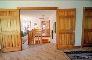 Un couloir au plancher de bois, avec des portes ouvertes donnant sur un espace de vie comprenant un canapé et un escalier.