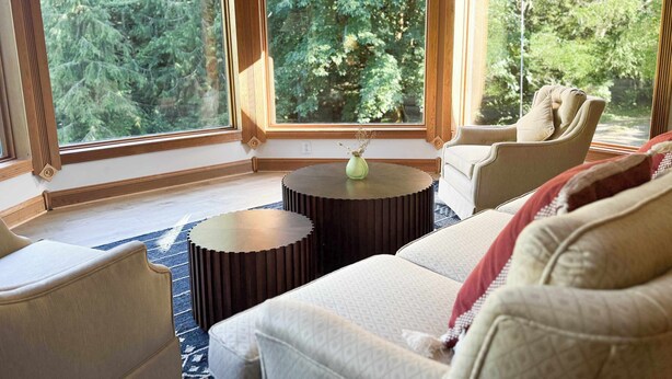 Un salon chaleureux avec une grande fenêtre, une table basse ronde et un canapé beige.